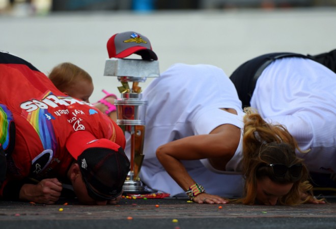 INDIANAPOLIS, IN - JULY 24:  Kyle Busch, driver of the #18 Skittles Toyota, kisses the bricks with his wife, Samantha, and son, Brexton, after winning the NASCAR Sprint Cup Series Crown Royal Presents the Combat Wounded Coalition 400 at Indianapolis Motor Speedway on July 24, 2016 in Indianapolis, Indiana.  (Photo by Bobby Ellis/Getty Images)